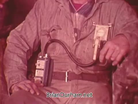 The still from the 'Mining Enforcement and Safety Administration PSA' features a miner sitting down, wearing a work uniform. The focus is on a device attached to his waist, which appears to be a safety instrument, possibly for monitoring air quality or other hazardous conditions in the mining environment. The image emphasizes the importance of safety equipment in the mining industry.