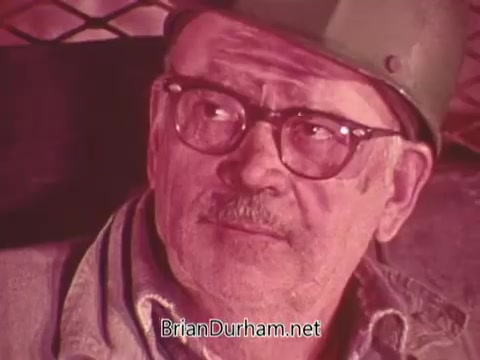 The still features an older man wearing a hard hat and glasses, looking pensively to the side. He has a weathered face, suggesting experience and concern. The color tones are muted, creating a serious atmosphere, likely reflecting the gravity of mining safety issues. This PSA emphasizes the importance of safety in mining operations.