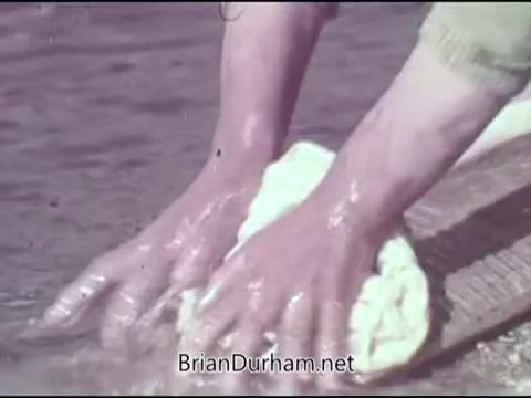 The still from the 'Christian Children's Fund PSA - 1969' shows a close-up of hands washing a cloth in water. The focus on the hands suggests a theme of care and support, aligned with the organization's mission to aid children. The image evokes a sense of community service and the importance of clean water and sanitation.