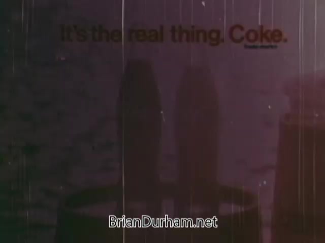 The still from the 1973 Coca-Cola nostalgia commercial features a simple yet evocative visual. It highlights the slogan 'It's the real thing. Coke.' against a backdrop that suggests a nostalgic ambiance, likely evoking themes of refreshment and authenticity. The imagery has a vintage quality, consistent with the era, likely enhancing the emotional appeal associated with Coca-Cola. The overall composition emphasizes the brand's iconic presence in popular culture.