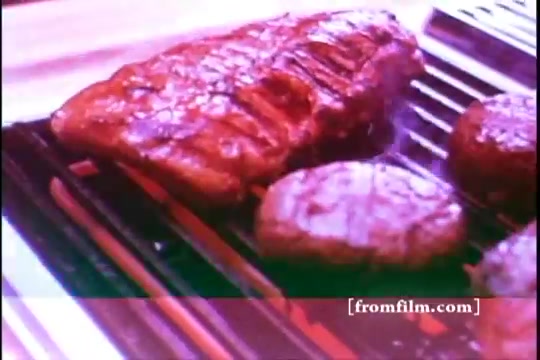 The still features a close-up of grilled meat on a Jenn Air grill, showcasing a juicy steak alongside several hamburger patties. The grilling surface is well-designed, emphasizing the cooking process. The vibrant colors and textures highlight the appeal of outdoor cooking typical of 1970s advertisements.