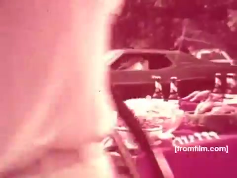 The still shows a vibrant outdoor scene likely depicting a gathering or picnic featuring Pabst Beer products. A table laden with food is prominent, while a vintage car is visible in the background. The colors have a warm, slightly faded look characteristic of 16mm film from the 1970s, enhancing the nostalgic feel of the commercial. The atmosphere suggests a casual, social setting centered around enjoying beer and good company.