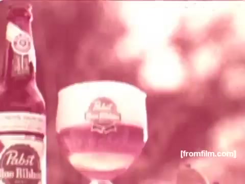 The still features a Pabst Beer bottle alongside a glass of beer, showcasing the beverage's branding. The glass is filled with a golden-colored beer, highlighting its frothy head. The overall aesthetic has a nostalgic hue typical of 1970s commercials, emphasizing the casual and enjoyable nature of the product. The background is likely to be outdoor, enhancing the theme of leisure and refreshment associated with drinking beer.