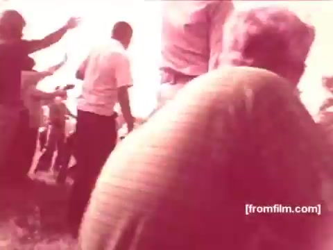 The still from the 16mm prints of 'Pabst Beer Commercials - 1970s' captures a lively outdoor scene. People are gathered, engaged in animated activity, perhaps celebrating or socializing, indicative of a joyful atmosphere. The image has a faded, vintage quality typical of the era, emphasizing a nostalgic feel associated with the brand's marketing approach during that time.