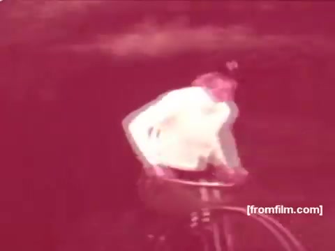 The 16mm still from the 'Pabst Beer Commercials - 1970's' features a person riding a vintage bicycle. The coloring appears warm and slightly faded, characteristic of the film era, creating a nostalgic atmosphere. The overall scene likely reflects the carefree lifestyle associated with enjoying Pabst Beer during that time period. The cyclist's attire and the setting evoke a sense of leisure and outdoor fun typical of 1970s advertisements.