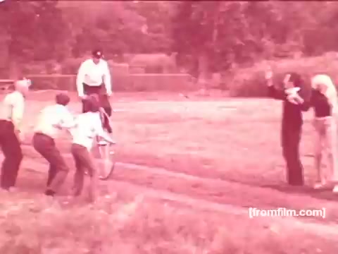 The still features a lively outdoor scene from a Pabst Beer commercial set in the 1970s. It shows a group of people, likely friends or family, engaging happily as one person rides a unicycle. The atmosphere is playful and energetic, capturing a moment of enjoyment and camaraderie. The colors appear muted, typical of 16mm film prints from that era.