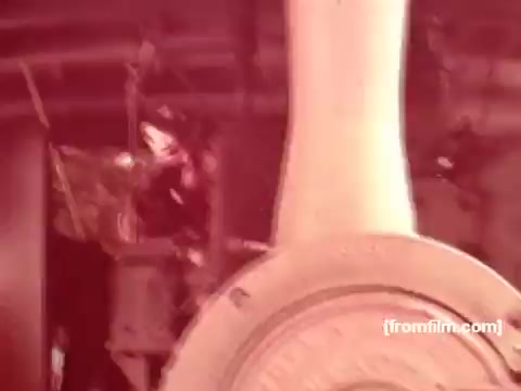 The still from the 'Pabst Beer Commercials - 1970s' features industrial machinery, likely from a brewing facility, with a prominent focus on a large wheel or gear. The image is tinted, giving it a warm, vintage feel characteristic of 16mm film. The setting suggests a nostalgic look at the brewing process, emphasizing the craftsmanship behind Pabst Beer during that era. The overall tone reflects a blend of tradition and industrial strength.