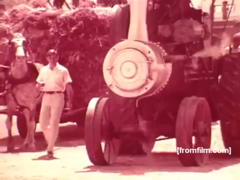 The still from the 'Pabst Beer Commercials - 1970s' shows a scene with a horse-drawn cart carrying hay, alongside a man in light clothing walking near a steam engine. The color tone has a warm, vintage feel typical of 16mm film from that era. The composition evokes a rustic, nostalgic connection to simpler times, possibly underscoring themes of traditional craftsmanship or rural life associated with the brand.