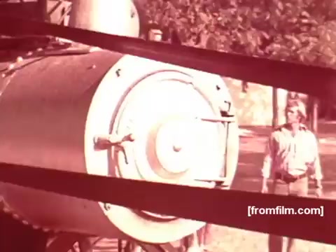 The still from the 16mm print of the 1970s Pabst Beer commercials features a man standing near a large industrial machine, likely a brewing apparatus. The image is characterized by a warm, nostalgic color palette typical of that era. The presence of the machine suggests a focus on the brewing process or the craftsmanship behind the beer, aligning with marketing themes of authenticity and tradition in beverage advertising.
