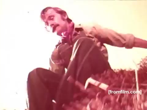 The still from the 16mm Pabst Beer commercials features a man sitting on a pile of hay or grass. He has a mustache and wears a shirt with rolled-up sleeves, paired with a bandana around his neck. The lighting appears warm, giving the scene a nostalgic and inviting feel typical of 1970s advertising. The overall atmosphere suggests a rural or outdoor setting, likely aligning with themes of simplicity and enjoyment associated with Pabst Beer.