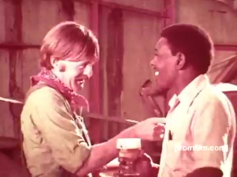 The still features two individuals, a man and a woman, engaging in a friendly conversation, likely promoting a sense of camaraderie associated with Pabst Beer. The setting appears casual with industrial elements in the background, reflecting a relaxed and approachable atmosphere typical of 1970s advertisements. The characters seem to be enjoying their time together, with a focus on sharing a beer, emphasizing social connections. The overall tone suggests a celebration of friendship and leisure.