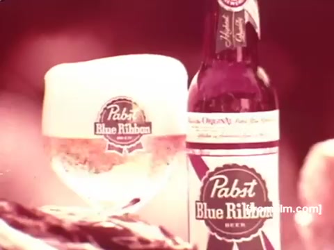 The still features a classic presentation of Pabst Blue Ribbon beer, showcasing a bottle and a glass filled with the beverage. The glass has a frothy top, emphasizing freshness. The background is softly blurred, likely highlighting the beer as the focal point. The iconic Pabst branding is prominently displayed on both the bottle and the glass, typical of 1970s beer advertisements. The overall color tone suggests a vintage aesthetic reflective of the era.