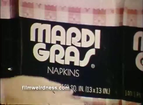 The still features a package of 'Mardi Gras Napkins,' prominently displaying the brand name in bold white letters against a black background. The napkin package is neatly arranged, with measurements stated as 13 inches by 13 inches. The overall aesthetic is simple yet attention-grabbing, reflecting the festive feel associated with Mardi Gras celebrations.