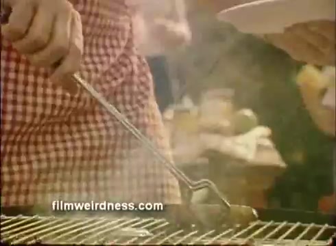 The still features a close-up of a person in a checkered apron using a grilling tool to handle food on a barbecue. The scene is filled with steam, suggesting a lively outdoor cooking environment typical of a festive gathering. The background is adorned with a blur of people, creating a joyful and communal atmosphere, in line with the Mardi Gras theme.