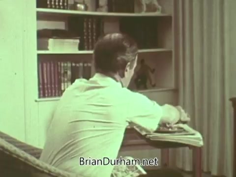 The still shows a person seated on a couch, appearing to be engaged in thought or contemplation. The setting includes shelves filled with books and decorative items, suggesting a home environment. The color tone has a vintage quality, typical of the 1960s, reflecting a casual atmosphere likely related to a message or discussion from the Episcopal Church.