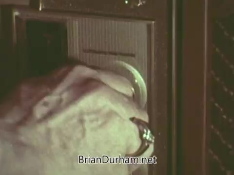 The still depicts a close-up hand turning a knob on a vintage radio or speaker system, suggesting the action of tuning in. The hand appears aged, hinting at a personal or communal connection to the broadcast, likely related to the PSA's themes. The overall visual aesthetic reflects a 1960s context.