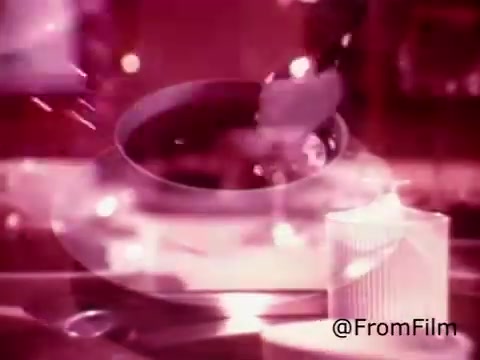 The still from the 'Coffee-Mate Commercial - Space Needle - 1970's' features a close-up of a coffee cup being filled, possibly with cream or a similar product. The setting has a vibrant, warm color palette, enhancing the nostalgic feel of the 1970s. There are soft, dreamy light reflections, contributing to a cozy atmosphere. The iconic Space Needle likely serves as a backdrop, highlighting the commercial's connection to Seattle. Overall, the imagery evokes a sense of indulgence and comfort associated with coffee drinking.