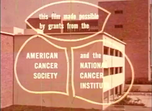 The still features text overlaid on a building, indicating that the film 'The Human Cell and the Cytologist' was funded by grants from the American Cancer Society and the National Cancer Institute. The visual style reflects the educational nature of the film, with emphasis on the importance of cancer research. The background shows a plain institutional structure, typical of educational film aesthetics from that era.