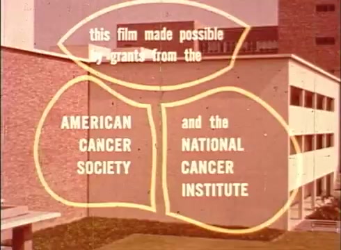 The still from 'The Human Cell and the Cytologist' features text within three overlapping circles. It credits the funding sources for the film, highlighting contributions from the American Cancer Society and the National Cancer Institute. The background shows a building, indicating an academic or research setting. The visual style is typical of educational films from that era, with bold, clear lettering on a muted background.