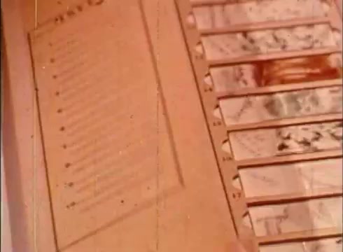 The still depicts a page from an educational film featuring a list, likely outlining key points or findings related to cytology. Adjacent to the text are several filmstrips, showcasing various microscopic images or diagrams pertinent to the study of human cells. The overall color tone is warm and slightly faded, characteristic of a 16mm print, emphasizing its vintage quality. The scene serves to illustrate the educational focus on cellular structures and their examination.