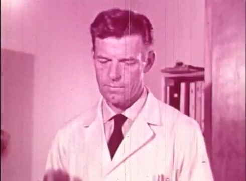 The still from 'The Human Cell and the Cytologist' features a male scientist in a lab coat, focused on an object in his hands. The image has a vintage quality, characteristic of 16mm film, with a pinkish tint and visible scratches or wear. The background suggests a laboratory setting, enhancing the educational context of the film, which likely explores aspects of cell biology and cytology.