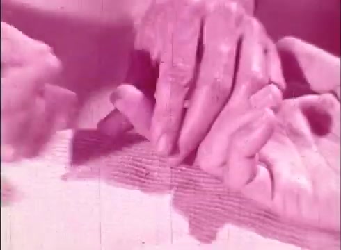 The still features close-up hands engaging with each other, likely illustrating a concept related to biology or cellular interaction. The visual tone is predominantly pink, characteristic of the film's era and possibly representing a specific theme or educational focus. The context suggests an emphasis on the human cell and its cellular processes, aiming to inform viewers about the intricacies of cellular function and structure in a tactile manner.