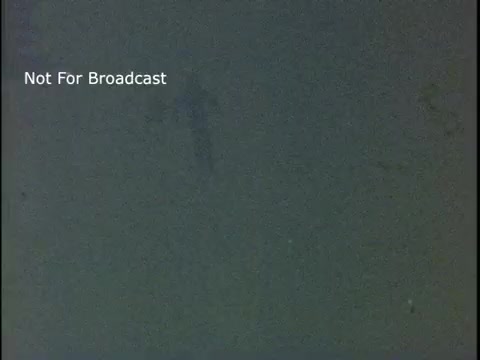 The still shows a dimly lit scene with a figure appearing to be in motion, likely representing physical activity as part of the public service announcement. The background is vague and suggests an emphasis on movement and fitness. The overlay text states 'Not For Broadcast,' indicating it's a restricted image from a promotional campaign featuring John Denver.