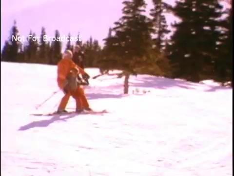 The still features two individuals skiing in a snowy landscape, dressed in colorful ski attire. The scene captures the essence of outdoor activity and physical fitness, reflecting the positive message of the John Denver PSA for the Presidents Council on Physical Fitness and Sports. The backdrop includes snowy trees and a clear sky, emphasizing a healthy and active lifestyle.