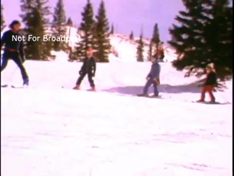 The still features a snowy landscape with several individuals skiing. They appear to be enjoying outdoor physical activity, embodying the spirit of fitness and wellness promoted in the PSA. Trees are visible in the background, enhancing the winter scenery. The overall tone conveys a message of promoting active lifestyles, particularly in winter sports.