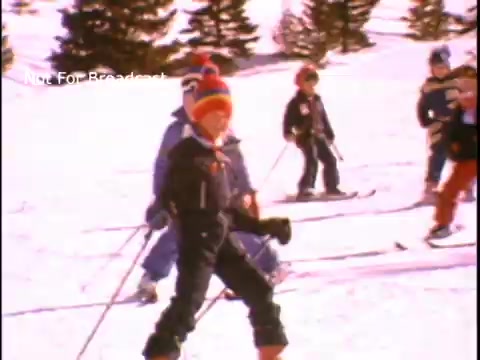 The still features a group of children skiing in a snowy environment, showcasing an active and playful atmosphere. They are dressed in colorful winter attire, reflecting the excitement of outdoor sports and physical fitness. The backdrop consists of snow-covered trees, emphasizing a winter sports setting. This scene is part of a public service announcement promoting physical fitness.