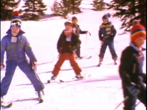 The still shows a group of children skiing in a snowy landscape, dressed in colorful winter gear. The scene reflects a focus on physical activity and outdoor sports, promoting a healthy lifestyle as part of the John Denver public service announcement related to the Presidents Council on Physical Fitness and Sports. Snow-covered trees in the background enhance the winter sports atmosphere.