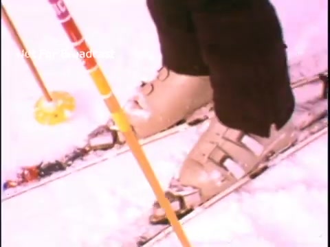 The still depicts a close-up of ski boots resting on ski equipment on snow. The boots are beige with buckles, and ski poles are visible nearby, suggesting an outdoor winter sports setting. This imagery aligns with the theme of promoting physical fitness and outdoor activities in the context of John Denver's PSA for the President's Council on Physical Fitness and Sports.
