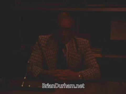 The still features a dimly lit scene of a man sitting at a desk, wearing a patterned blazer. The atmosphere appears serious and formal, likely indicating a political message. This is part of a political advertisement opposing Issue Six related to nuclear power in Ohio. The low lighting may suggest an ominous tone, typical of campaign strategies aimed at influencing voter opinion.
