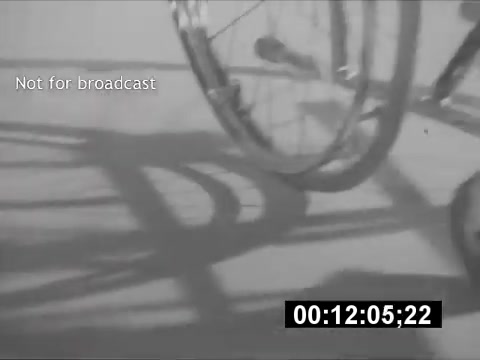 The still from the 16mm print features the shadow and parts of a wheelchair in monochrome. The image is slightly blurred, focusing on the wheel and its shadow against a light background. A timestamp indicates the footage runs for 12 seconds and 5 frames. The text 'Not for broadcast' is displayed prominently, suggesting a behind-the-scenes or archival aspect. The overall composition conveys a sense of movement and simplicity.
