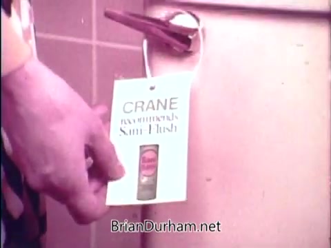 The still features a hand holding a tag that advertises 'Sani Flush,' a cleaning product designed to eliminate household germs in 15 seconds. The tag is attached to a bathroom fixture, likely emphasizing cleanliness. The overall tone suggests a focus on sanitation and quick effectiveness.