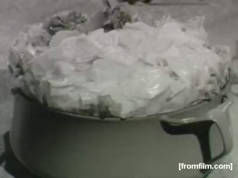 The still features a pot filled with a creamy potato salad, topped with layers of sliced ingredients. The visual suggests a wholesome, comforting meal typical of the late 1950s to early 1960s, highlighting the era's home cooking and family gathering themes. The monochrome color adds a nostalgic quality to the scene.