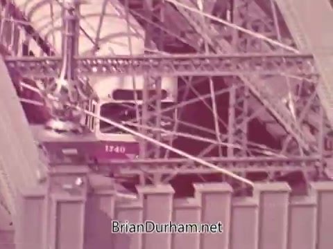 The still features a segment from an Iron City Beer commercial, showcasing a cityscape with a prominent industrial or urban setting. The visual emphasizes structural elements, likely conveying a local pride and connection to the beer. The use of 16mm film suggests a vintage aesthetic, aligning with the retro feel of the commercial.