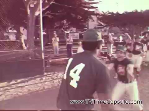 The still shows a group of children playing baseball, with one player wearing a green cap and jersey number 14. The scene captures a lively outdoor game atmosphere, likely during a sunny day, with spectators in the background. This image is part of a 1978 7-Up commercial, evoking themes of fun and youthfulness.