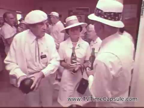 The still features people dressed in white attire, likely representing a social gathering or event, engaging in conversation. They hold bottles of 7-Up, emphasizing the beverage's presence in a friendly, relaxed atmosphere. The vintage style and clothing reflect the era of the late 1970s. The scene conveys a lighthearted, communal vibe typical of advertisements from that time.