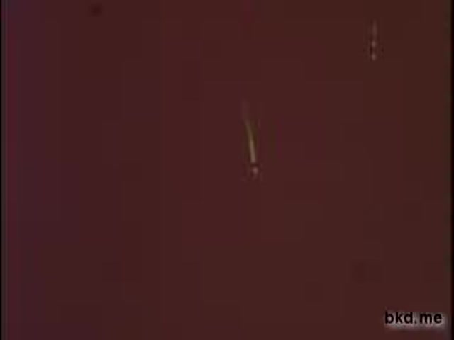 The still from the 'Lucky Draft Beer' commercial features a warm, reddish background with a subtle golden line, possibly indicating movement, reminiscent of pouring or serving beer. The image has a vintage quality, characteristic of a 16mm print, with soft focus and graininess enhancing its nostalgic feel.