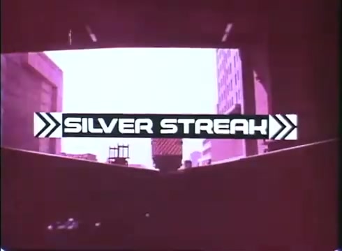 The still from the trailer for 'Silver Streak' features the film's title prominently displayed in bold, stylized lettering. The background shows a view through an arched opening, likely from a train or urban environment, with city buildings visible. The overall color tone has a vintage quality, characteristic of a 16mm print, with a slight pinkish hue. The design includes arrows that suggest movement, reinforcing the film's dynamic and adventurous theme.