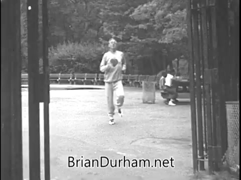 The still from the 1960s Heart Fund PSA featuring Ray Bolger as the Scarecrow depicts a park scene. A man is jogging through an open gate, dressed in casual athletic wear, suggesting a focus on heart health and physical fitness. The background includes park benches and greenery, emphasizing an active lifestyle. This aligns with the PSA's message promoting heart health awareness.