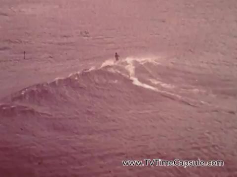 The still from the 'Army Recruiting Commercial - Your Man in Waikiki' showcases a surfer riding a wave in a tranquil ocean scene. The setting appears vibrant and dynamic, capturing the spirit of leisure and adventure typically associated with Waikiki. The colors suggest a warm, nostalgic atmosphere, emphasizing the appealing lifestyle that the commercial likely aims to convey.
