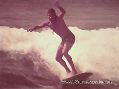 The still from 'Army Recruiting Commercial - Your Man in Waikiki' features a young man surfing, showcasing a dynamic moment as he rides a wave. The scene captures the essence of a beach lifestyle in Waikiki, emphasizing leisure and adventure. The warm color tones give it a nostalgic feel typical of the era. This imagery connects the themes of the military with the vibrant, active lifestyle often associated with Hawaii.