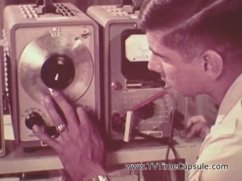 The still features a young serviceman operating a piece of electronic equipment. He is focused on adjusting a dial on one of the devices, which appears to be part of a technical setup, perhaps for communication or surveillance. His hand, adorned with a ring, suggests a casual yet serious demeanor. The overall context indicates a promotional message about the opportunities available in the Army, highlighting technical skills and career prospects.