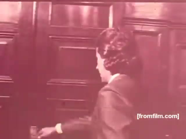 The still likely depicts a woman in 1970s attire, opening a door, suggesting a theme of sophistication or invitation commonly used in advertisements. The warm, muted color palette is characteristic of the era, enhancing a nostalgic feel. This setting may evoke ideas of social gatherings or intimacy, which were often highlighted in cigarette commercials of that time, particularly for brands like Albany and Richmond. The overall composition likely aims to attract a target audience by emphasizing elegance and lifestyle.