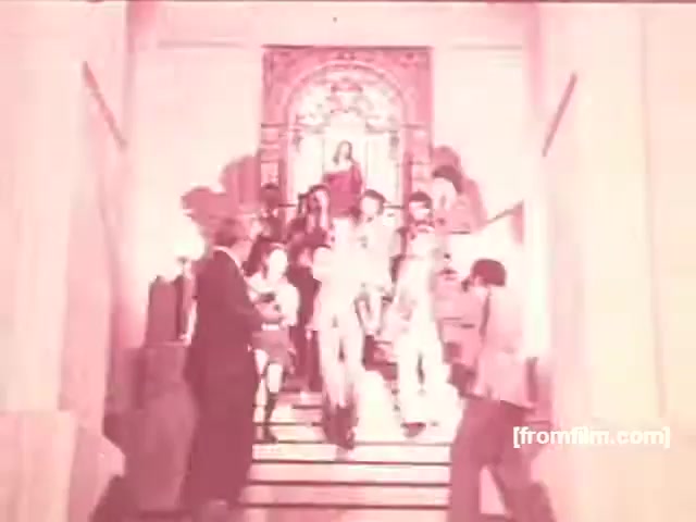 The still from the Souza Cruz Brazilian cigarette commercials features a group of stylishly dressed individuals descending a staircase in a grand setting. The warm, nostalgic color palette evokes the 1970s era, highlighting a social atmosphere. The scene captures an air of sophistication and camaraderie, typical of advertising from that time, aimed at promoting brands like Albany and Richmond.