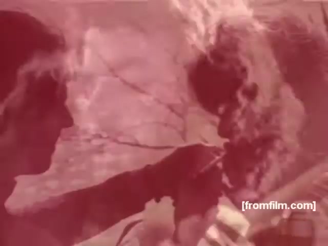 The still from the Souza Cruz Brazilian cigarette commercials of the 1970s features two figures in a warm, reddish tint. One person appears to be handing a cigarette to the other, emphasizing the social aspect of smoking. The background suggests an outdoor setting, likely aimed at portraying a relaxed, carefree lifestyle associated with the brands Albany or Richmond. The visual style reflects the aesthetic of the time, blending intimacy and a sense of camaraderie.