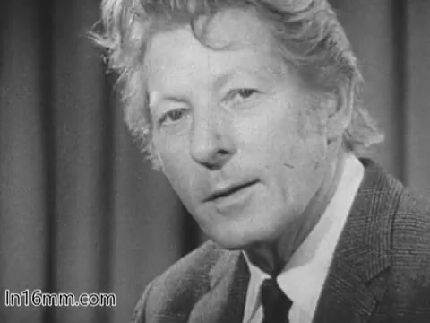 The 16mm still features Danny Kaye in a UNICEF public service announcement from the 1960s. He appears to be speaking directly to the camera, dressed in a suit with a tie. His expression is earnest, reflecting the serious nature of the message. The background has a simple, draped design, likely intended to keep the focus on Kaye and his appeal for UNICEF's mission.