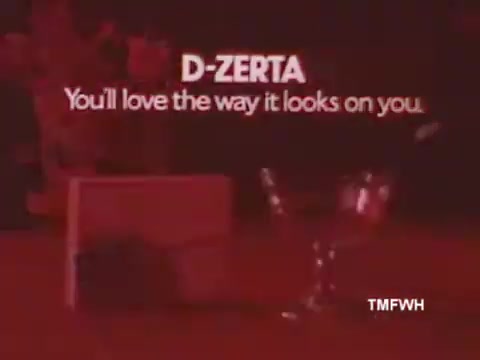 The still features a bold, white text slogan for D-Zerta: 'You'll love the way it looks on you' against a vibrant, red background. A glass and possibly a dessert container are subtly visible, emphasizing the product's appeal. The visual style suggests a playful and enticing atmosphere typical of 1970s-1980s advertising. The simplicity of the image focuses on branding and product presentation.